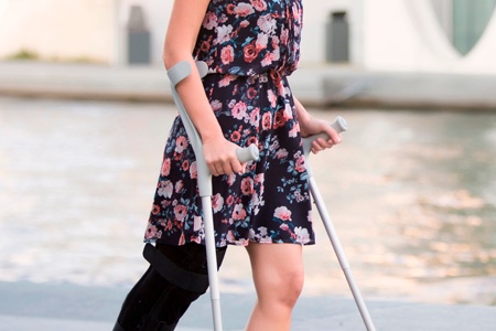 Une femme marche avec deux cannes anglaises classiques, les deux mains occupées par les poignées.